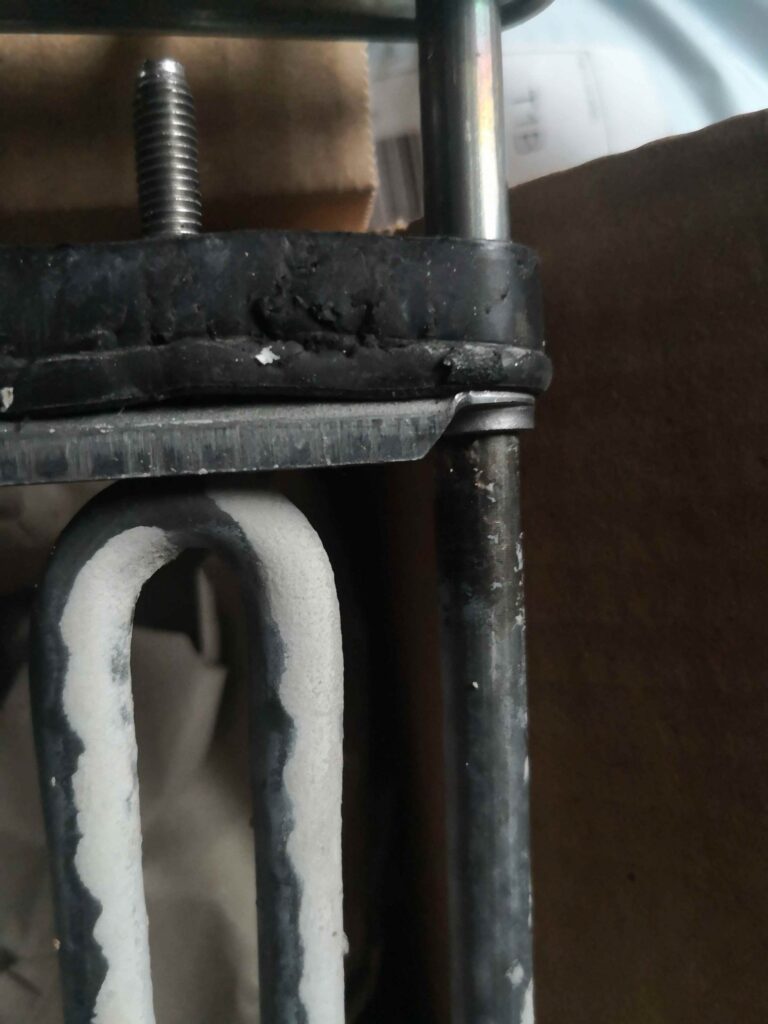 Zbliżenie na uszkodzoną grzałkę z miejscem na czujnik w pralce Hotpoint Ariston AWM 108 EU